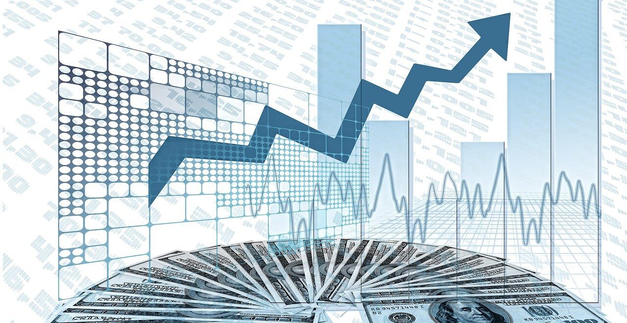 Δεκάδες χαρτονομίσματα των 100 δολαρίων απλωμένα σε ημικύκλιο μπροστά από ψηφιακά γραφήματα με μπλε ράβδους και βέλος που ανέρχεται.