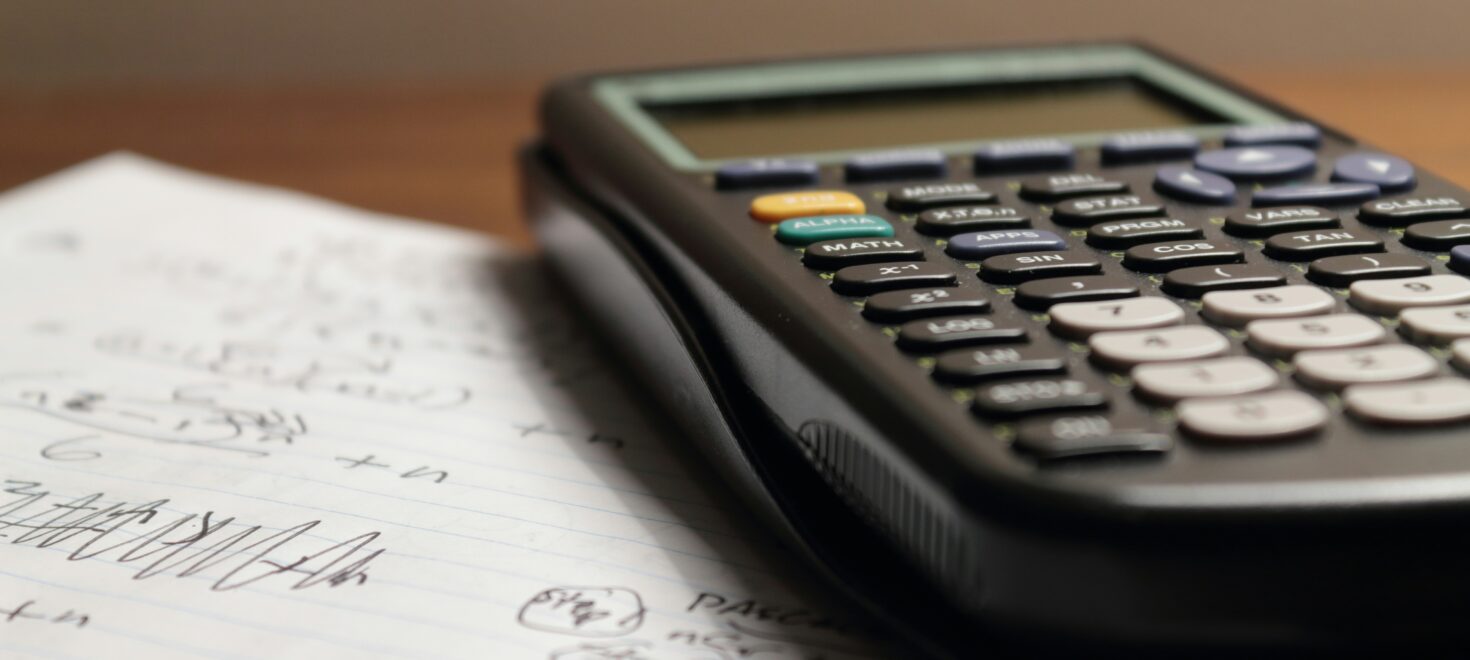 Μαύρη επιστημονική αριθμομηχανή τοποθετημένη πάνω σε φύλλο χαρτιού με χειρόγραφες σημειώσεις και μαθηματικές εξισώσεις.